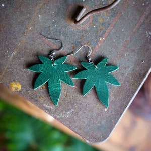 May include: A pair of green leather earrings shaped like maple leaves. The earrings have silver hooks.