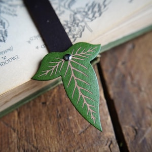 May include: A green leather bookmark shaped like a leaf with a silver rivet. The bookmark is on top of a book with a map printed on the pages.