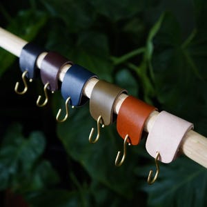 May include: A set of seven leather curtain tiebacks with brass hooks in various colors, including brown, navy blue, olive green, orange, and pink.