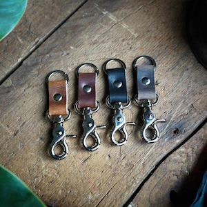 May include: Four leather keychains with silver swivel clips. The keychains are brown, dark brown, black, and light brown.