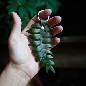 Agreen leather fern keychain is being held to show the size.