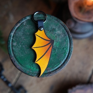 Peut inclure: Un porte-clés en cuir en forme d'aile de dragon jaune et orange avec une boucle en cuir noir et un anneau de clé argenté.