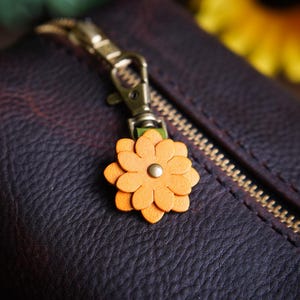 May include: A brown leather zippered pouch with a gold zipper and a small orange flower charm attached to the zipper pull.