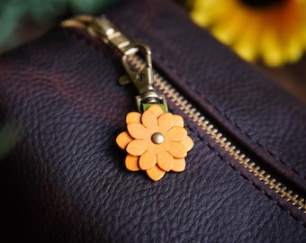 May include: A brown leather zippered pouch with a gold zipper and a small orange flower charm attached to the zipper pull.