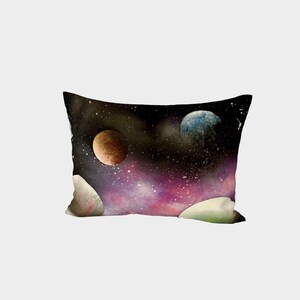 Op de afbeelding: Rechthoekig kussen met een ruimtethema-ontwerp. Het kussen heeft een donkere achtergrond met een levendige nevel in paarse en roze tinten. Verschillende planeten in bruine en blauwe tinten zijn zichtbaar, samen met witte sterren.