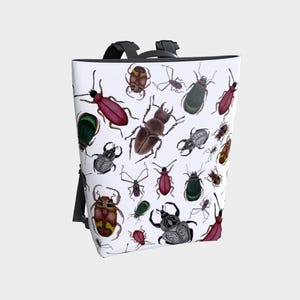 May include: White backpack with a repeating pattern of colourful beetles. The insects are in shades of red, brown, green, and grey. The backpack has black straps and a handle.