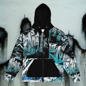 May include: A black zip-up hoodie with a hood and a front pocket. The hoodie features a graffiti-style design in shades of blue, white, and gray. The hood and pocket are solid black.