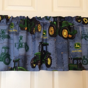 May include: A blue denim valance with a patchwork design featuring multiple green John Deere tractors. The valance has a white rod pocket and is perfect for a farm-themed nursery or bedroom.