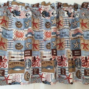 May include: A blue and brown fabric valance with a nautical theme. The fabric features a repeating pattern of seashells, starfish, anchors, and other nautical imagery. The valance is trimmed with a brown ruffle.