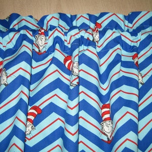 May include: Blue and light blue chevron patterned fabric with red stripes. The fabric features illustrations of a cat wearing a red and white striped hat. The fabric is gathered at the top, suggesting it is a curtain or valance.