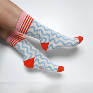 May include: A pair of white socks with a blue wavy pattern and red and pink stripes at the top. The socks have red heels and toes.