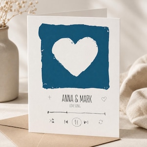 Könnte beinhalten: Eine weiße Grußkarte mit einem dunkelblauen Quadrat und einem weißen Herz-Ausschnitt. Unter dem Quadrat steht der Text ANNA & MARK und LOVE SONG, gefolgt von einer handgezeichneten Musik-Player-Oberfläche mit Fortschrittsbalken.