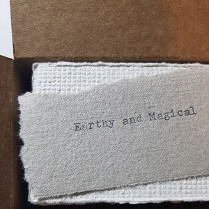 May include: A close-up of a white card with the text "Earthy and Magical" printed in black ink.