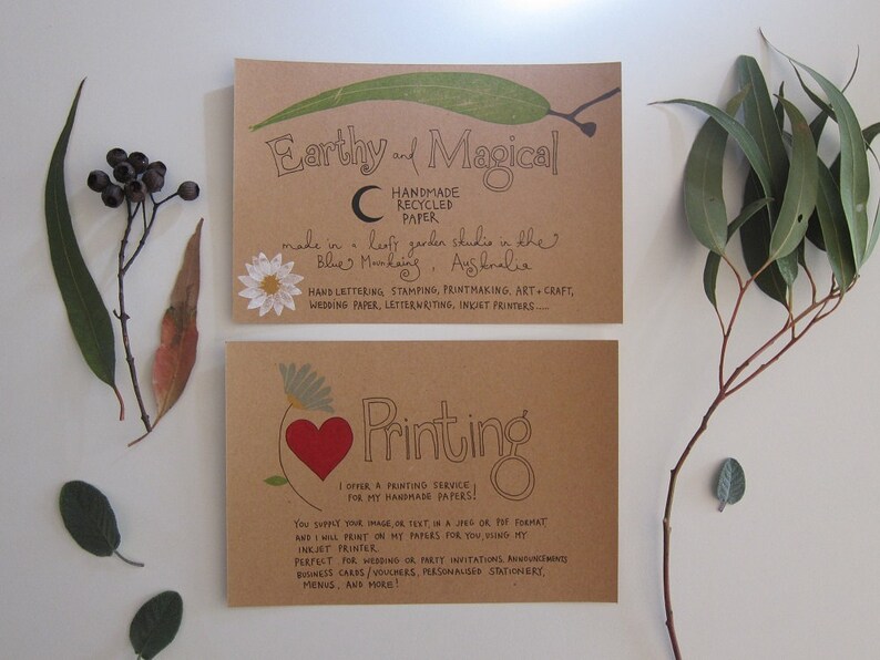 May include: Two brown cards with handwritten text on them. The top card says "Earthy and Magical" and "Handmade Recycled Paper." The bottom card says "Printing" and "I offer a printing service for my handmade papers!"