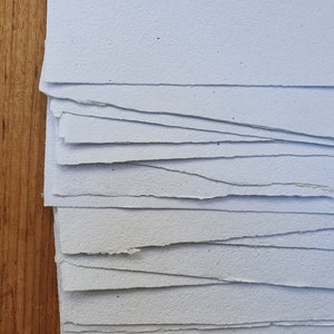 May include: A stack of white paper sheets with uneven edges. The paper has a speckled texture.