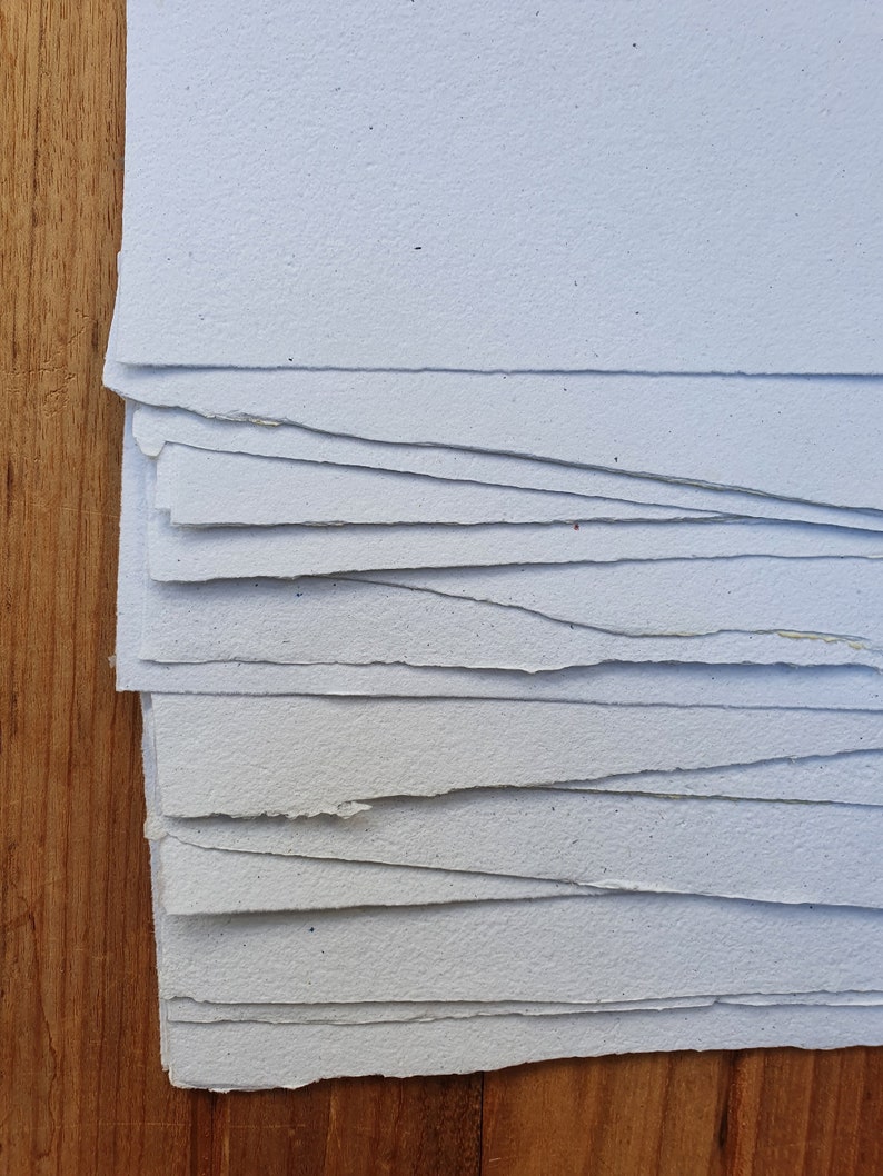 May include: A stack of white paper sheets with uneven edges. The paper has a speckled texture.