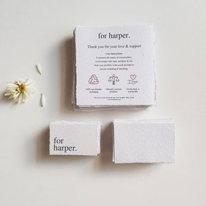 May include: A stack of white cards with the text "for harper. Thank you for your love & support" and care instructions for jewelry. The cards are made of recycled paper and feature icons for eco-friendly packaging, ethically sourced jewelry, and giving back to nonprofits.