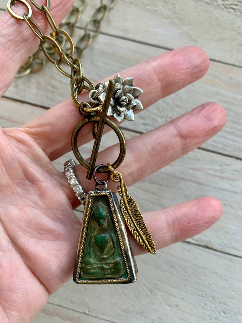 Zen 28\u201d long. Sitting Buddha pendant with feather and lotus dangles on brass chain and toggle
