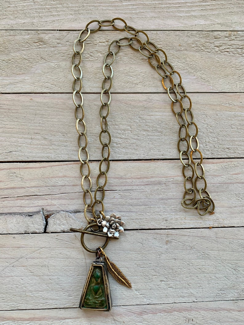 Zen 28\u201d long. Sitting Buddha pendant with feather and lotus dangles on brass chain and toggle