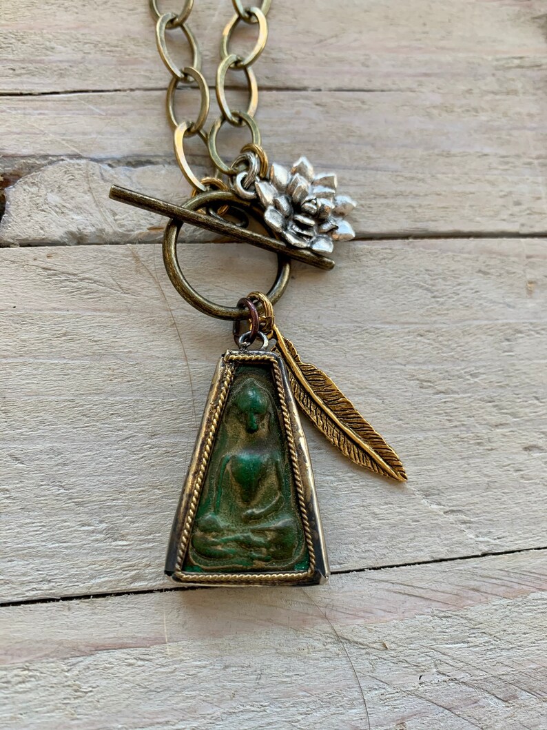 Zen 28\u201d long. Sitting Buddha pendant with feather and lotus dangles on brass chain and toggle