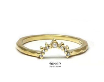 May include: A gold ring with a hammered texture featuring a curved arch design. The arch is set with small clear stones and a single central pearl. The text DINAR Jewelry design is printed below the ring in a black serif font on a white background.
