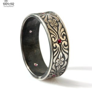 May include: A silver band ring with an intricate floral design and red gemstones. The ring is oxidized for a vintage look.