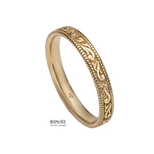 May include: A gold ring featuring an ornate floral design. The band is decorated with a detailed pattern and a border of small dots. The ring is set against a white backdrop. The text "DINAR jewelry design" is visible.