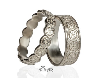 May include: Two silver wedding bands with intricate floral designs. The bands are stacked on top of each other.