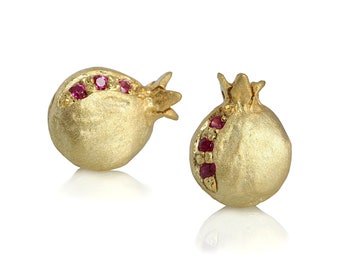 May include: A pair of gold pomegranate-shaped earrings with a matte finish. Each earring features a vertical row of small, round, vibrant red gemstones embedded along the side, mimicking the appearance of pomegranate seeds.