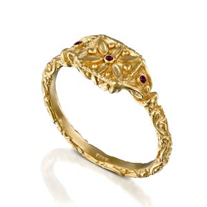 May include: A gold ring with a detailed floral design and three red gemstones. The ring is marked "925K" on the inside.