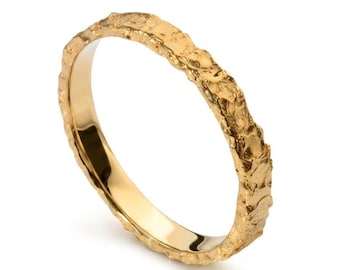 May include: A gold ring featuring a highly textured, rugged outer surface that contrasts with a smooth, polished interior band. The metal has a bright, reflective yellow gold finish, creating a distinct appearance with irregular, jagged edges.