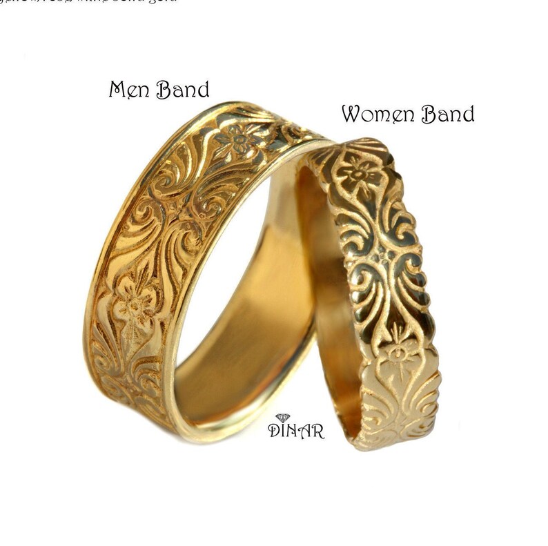 Pu&ograve; includere: Due anelli in oro con un'intricata incisione floreale e a volute. La fascia pi&ugrave; grande &egrave; etichettata Men Band e quella pi&ugrave; piccola Women Band. Il testo DINAR con un'icona a forma di diamante &egrave; visibile al centro in basso dell'immagine.