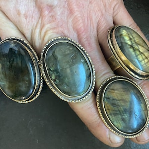 Puede incluir: Tres anillos ovalados con engaste de oro y una piedra de labradorita verde y dorada.