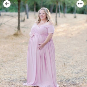 May include: A pregnant woman wearing a light pink off-the-shoulder maxi dress. She is standing in a field of dry grass.