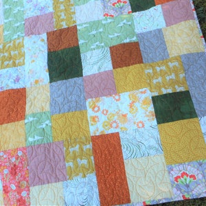 May include: A patchwork quilt with a variety of colorful fabrics, including green, orange, yellow, and pink. The quilt is made up of squares and rectangles, and the fabric patterns are floral, geometric, and abstract.