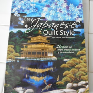 May include: Book cover with a gold and black illustration of a Japanese temple with a pond and koi fish. The title is "Easy Japanese Quilt Style" with the authors' names "Julia Davis & Anne Muxworthy" below. The subtitle is "10 stylish but simple projects inspired by Japanese fabric".