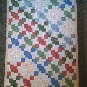 May include: A quilt with a patchwork design featuring squares of red, blue, green, and white fabric. The quilt is framed with a dark green border.