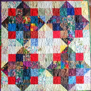 May include: A colourful quilt with a patchwork design featuring red, blue, green and white squares. The quilt is quilted with a swirling pattern.