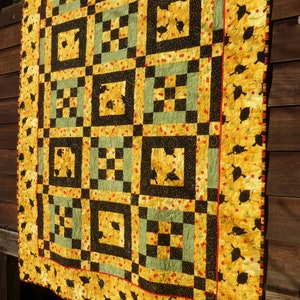 May include: A yellow and black quilt with a geometric pattern. The quilt is made of squares and rectangles, and it features a repeating design of black silhouettes of birds.