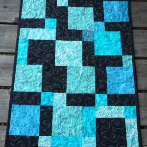 May include: A quilt with a black background and blue and teal squares. The squares are arranged in a random pattern and the quilt is quilted with a swirl design.