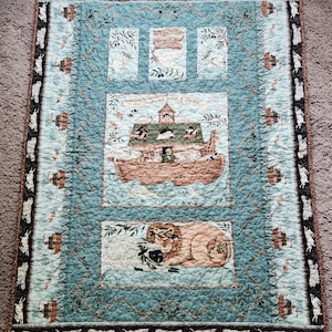 May include: A blue and brown quilted fabric with a Noah's Ark theme. The fabric features images of animals, a boat, and the text "All creatures great & small" and "All things wise & wonderful".