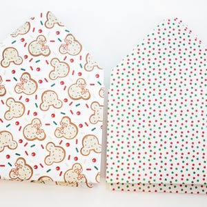 Puede incluir: Dos bolsas de regalo plegadas. Una presenta un patrón de galletas con forma de pan de jengibre con lazos rojos, chispas y puntos sobre un fondo blanco. La otra tiene un patrón de puntos rojos y verdes sobre un fondo blanco.