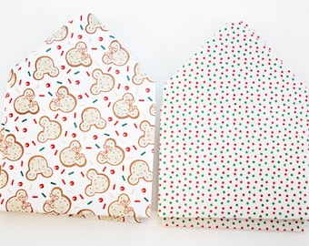 May include: Two folded gift bags. One features a pattern of gingerbread-shaped cookies with red bows, sprinkles, and dots on a white background. The other has a pattern of red and green dots on a white background.