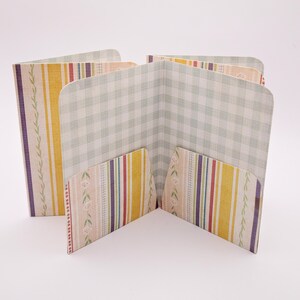 May include: A multi-pocket paper organizer with a variety of patterns. The organizer features a light green gingham pattern, vertical stripes in yellow, purple, and red, and a floral pattern. The pockets are open and angled.