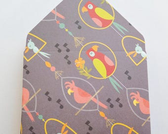 May include: A gray, house-shaped card with a repeating pattern of parrots in cages, musical notes, and decorative elements. The parrots are red, yellow, and pink, with blue and yellow birds in cages. The card has a white background.