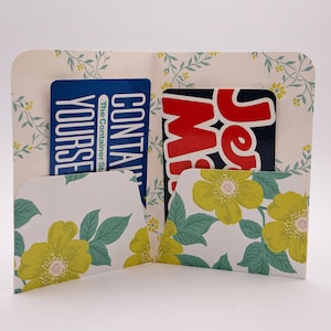 Może przedstawiać: Zestaw trzech ceramicznych kubków z nakrapianym, matowym wykończeniem. Kubki są w odcieniach kremu, jasnoszarym i ciemnoszarym. Każdy kubek ma prosty, minimalistyczny design i zaokrąglony uchwyt.