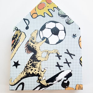 May include: A house-shaped card with a pop art style design. The card features a dinosaur on a skateboard, a soccer ball, pizza, musical notes, and stars. The background is light gray with small white dots.