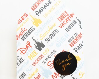May include: A white, house-shaped gift box with a colorful pattern of words and phrases like "Adventure," "Magic," and "Sunshine." A black circular sticker with "thank you" in gold script is affixed to the box.