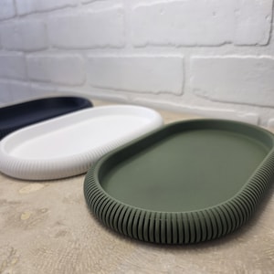 Puede incluir: Primer plano de tres bandejas decorativas ovaladas en diferentes colores. La bandeja delantera es verde oliva, la del medio es blanca y la trasera es azul marino. Cada bandeja tiene un borde acanalado.