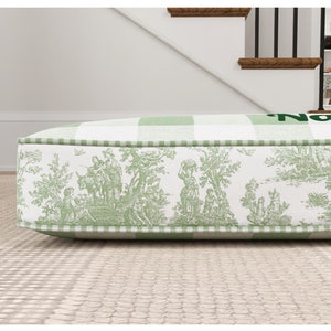 May include: A green and white checkered cushion with a toile pattern border. The cushion has the word "Nap" printed on it.